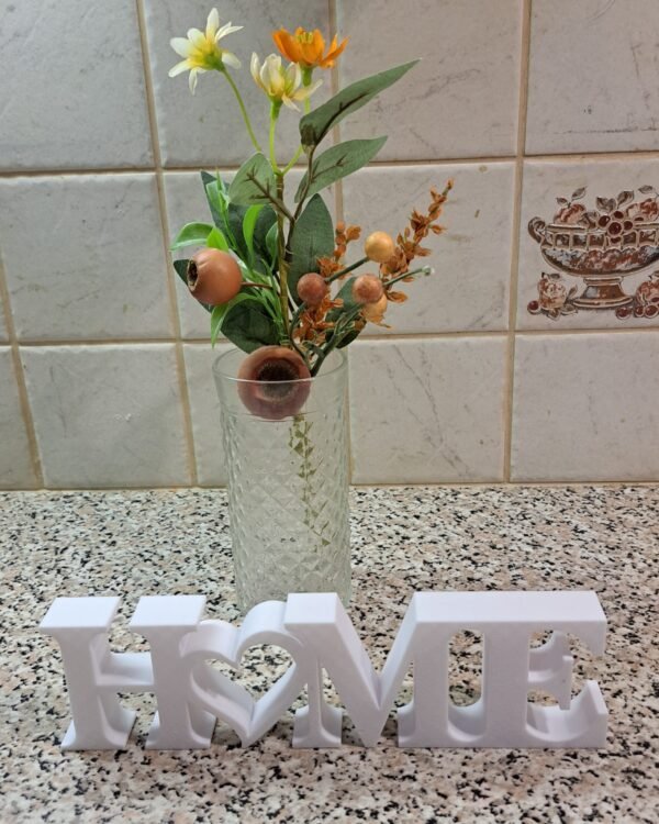 Valkoinen HOME-koriste sydämellä, koristeellinen tekokukkakimppu lasimaljakossa