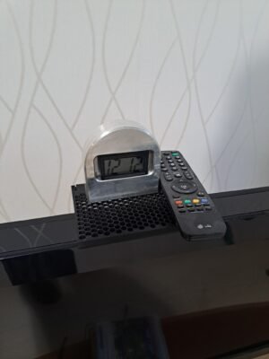 TV:n päälle asennettu 3D‑tulostettu hylly kellolle ja kaukosäätimelle