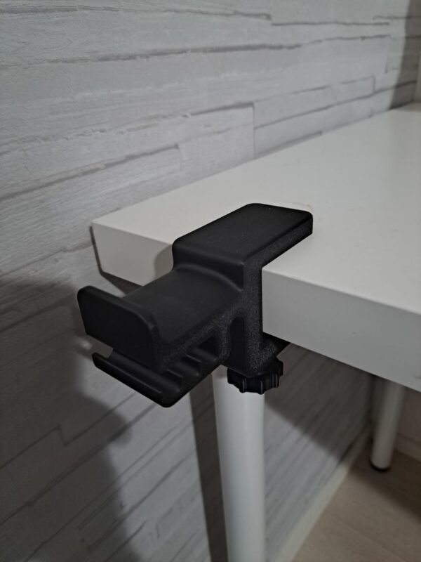 Musta pöydän reunaan kiinnitettävä kuuloketeline ilman kuulokkeita valkoisen pöydän kulmassa.