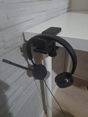 Musta pöydän reunaan kiinnitettävä kuuloketeline, jossa kuulokkeet roikkuvat.