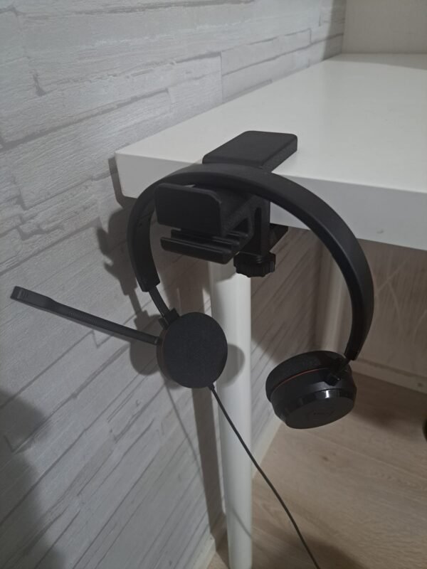 Musta pöydän reunaan kiinnitettävä kuuloketeline, jossa kuulokkeet roikkuvat.