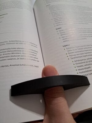 Musta kirjan sivunpidin käytössä peukalossa avoimen kirjan kanssa